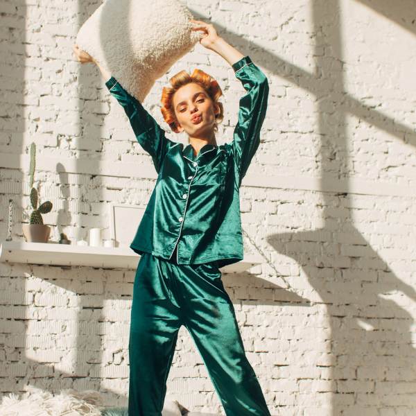 Woman in emerald pajamas with a silky feel holds a pillow overhead, setting up the question of whether mulberry silk is real silk.